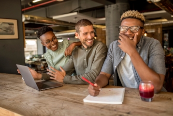 Three smiling friends in a cafe with laptops