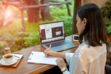 A woman writing a letter near her laptop