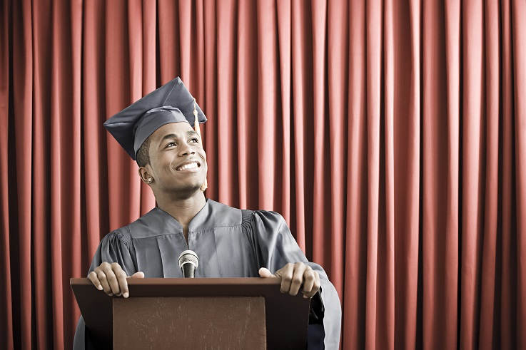 Photo of a young man wearing a graduation robe and standing at a podium.