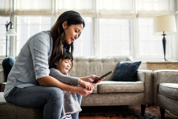 A mother looking at her phone with her young daughter