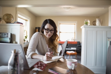 Woman writing in journal at dining table